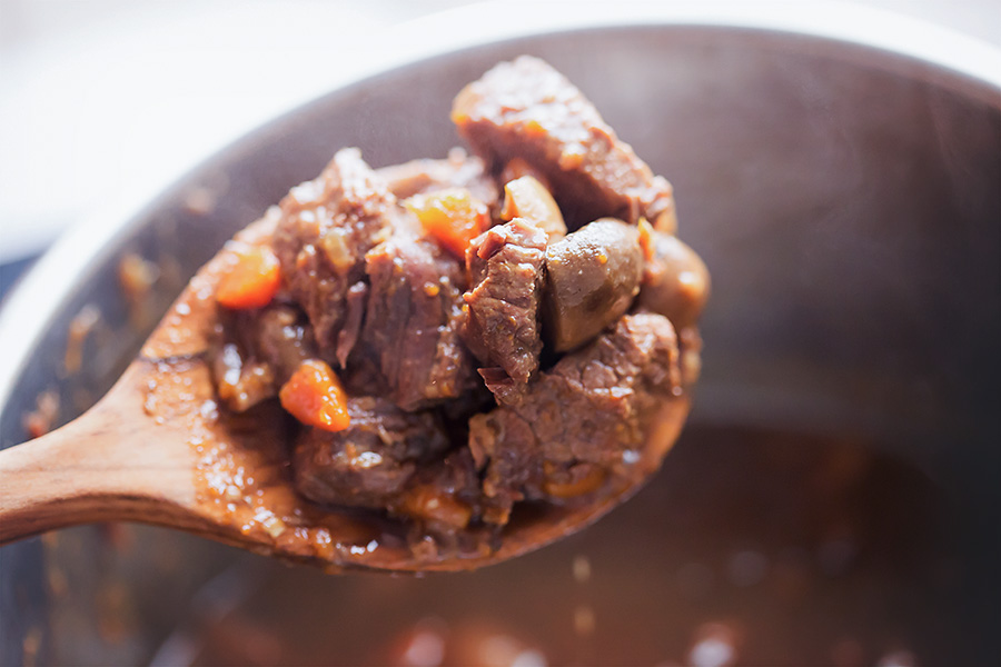 a serving spoon full of beef tips with mushrooms and carrots.