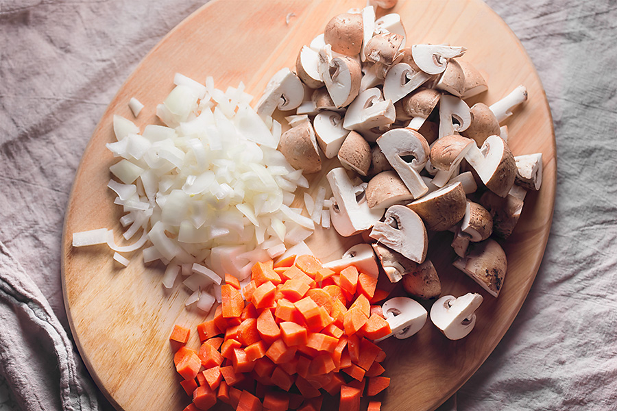 a pile of diced onions, diced carrots, and quartered mushrooms on a cutting board